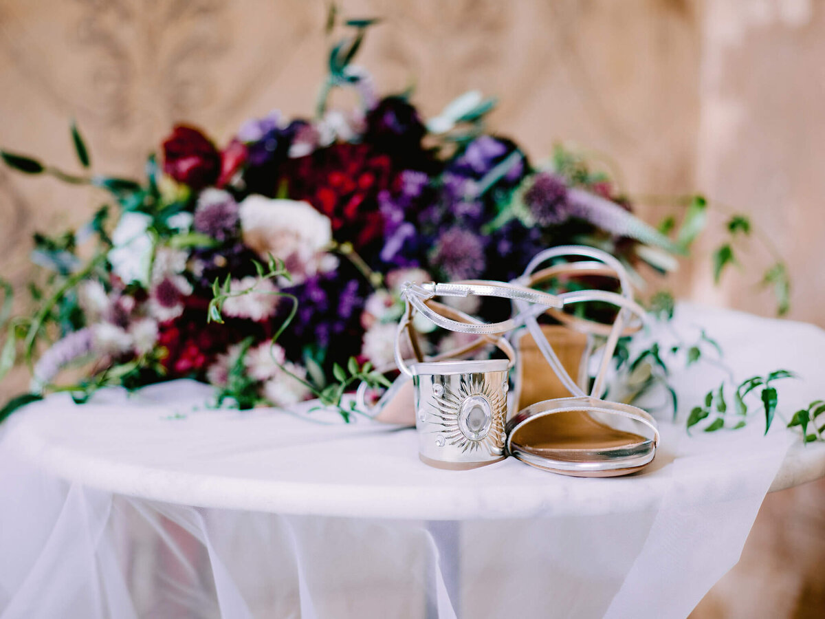 Wedding shoes on a table, with a flower bouquet on the background