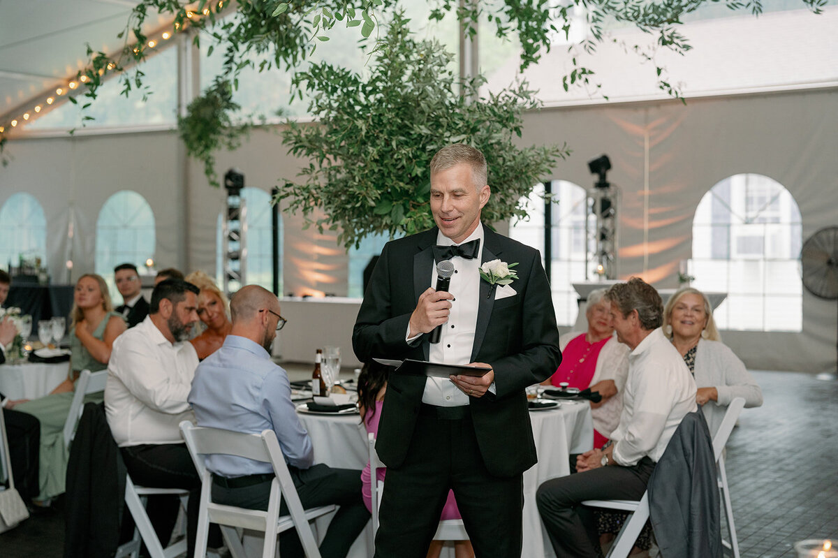 Groom giving a toast during their Morris Estate wedding reception under greenery and string lights.