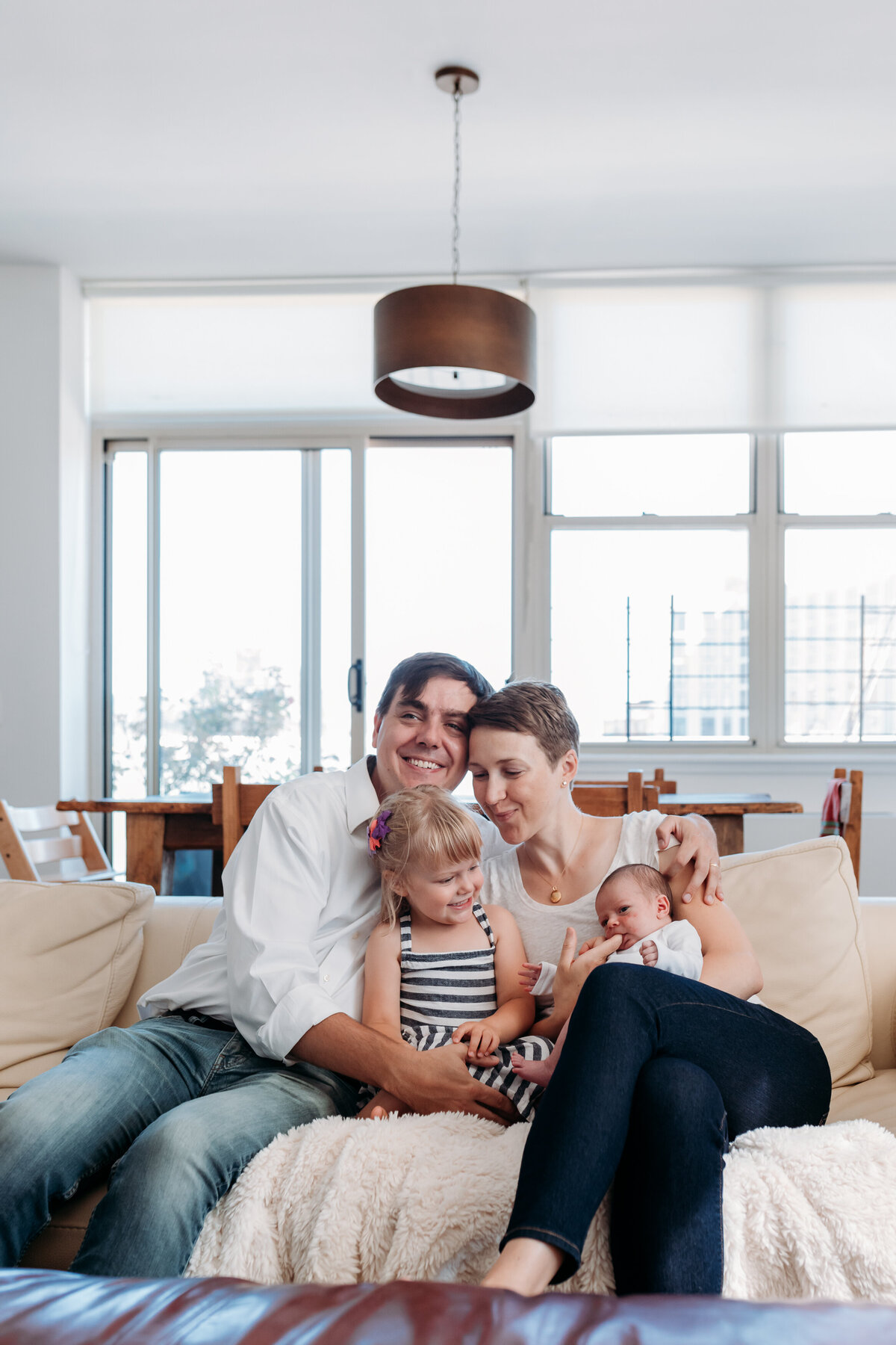 Newborn Photographer, a small family leans into each other on the couch with baby