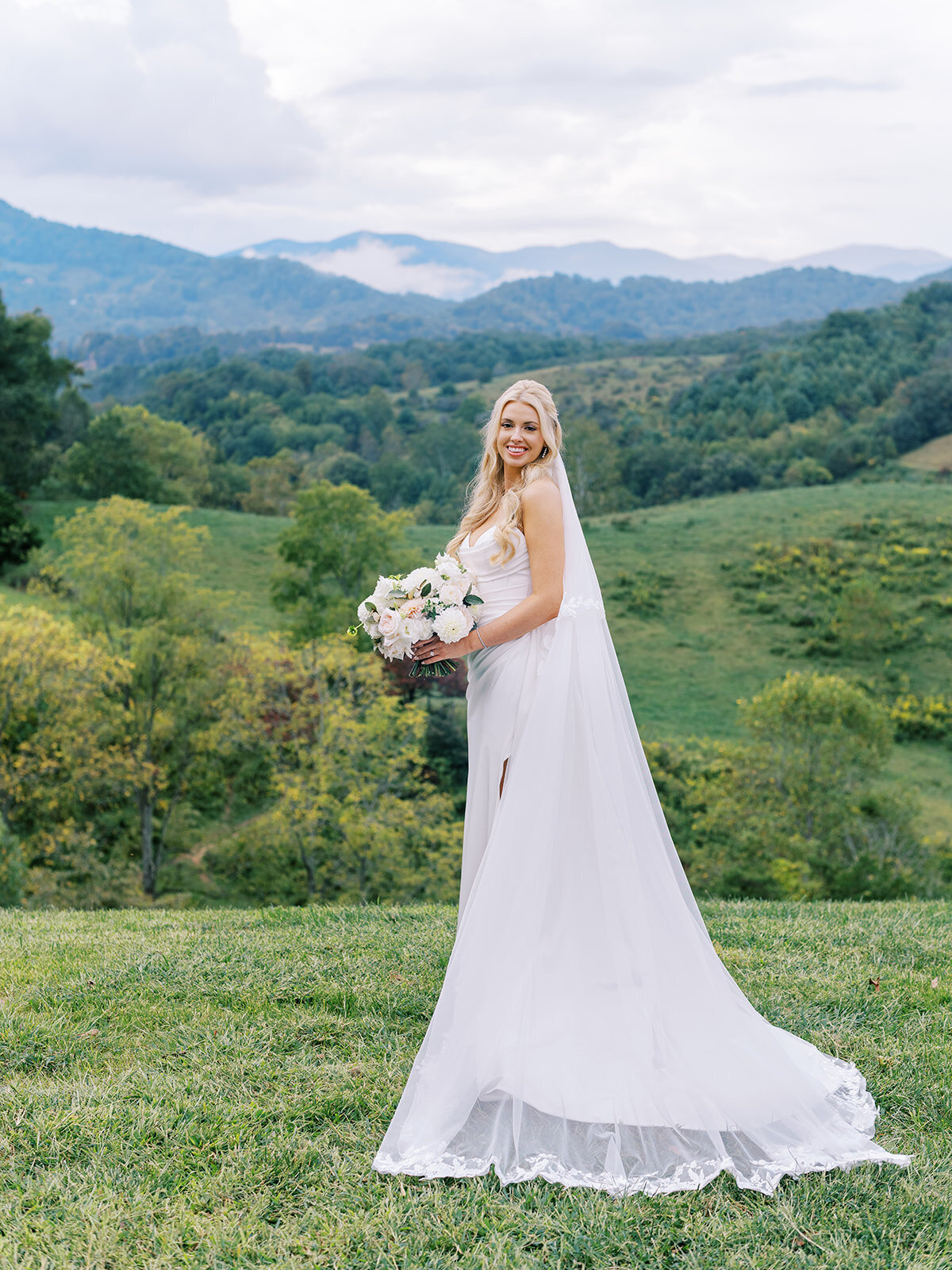 Bride holding bouquet with flowing veil, standing against mountain views at Waynesville Inn and Golf Club.