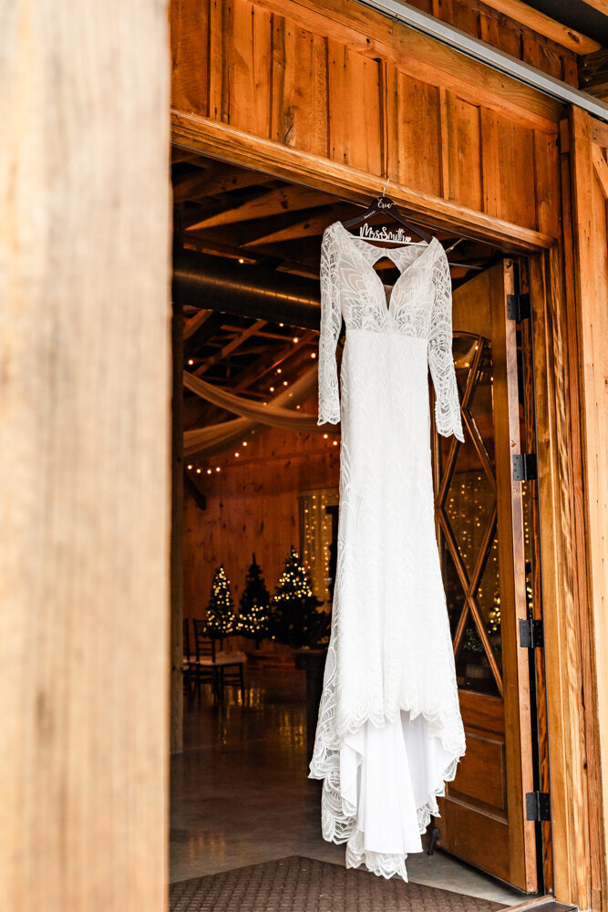 Brides elegant long sleeved gown hanging from a rustic entranceway