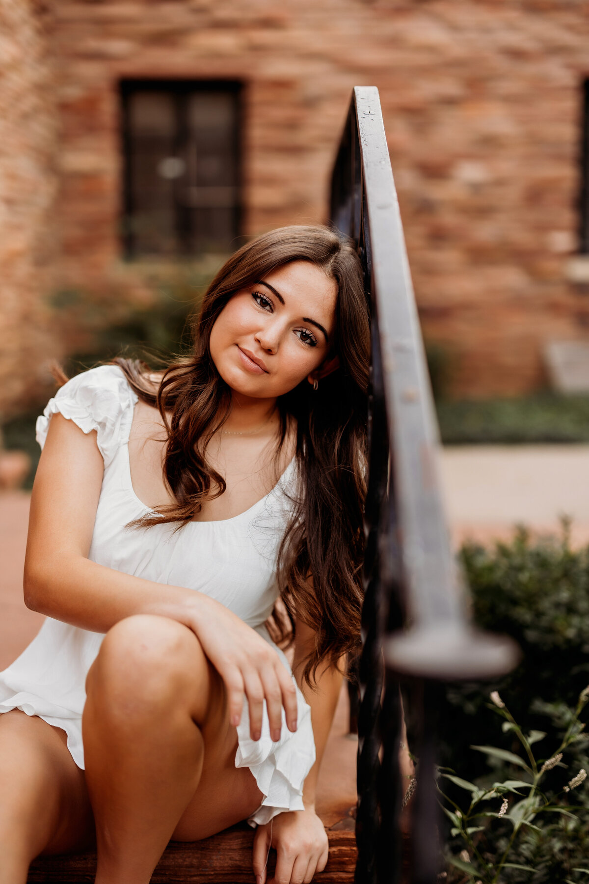 High school girl senior poses on a set of steps while resting her head on metal railing