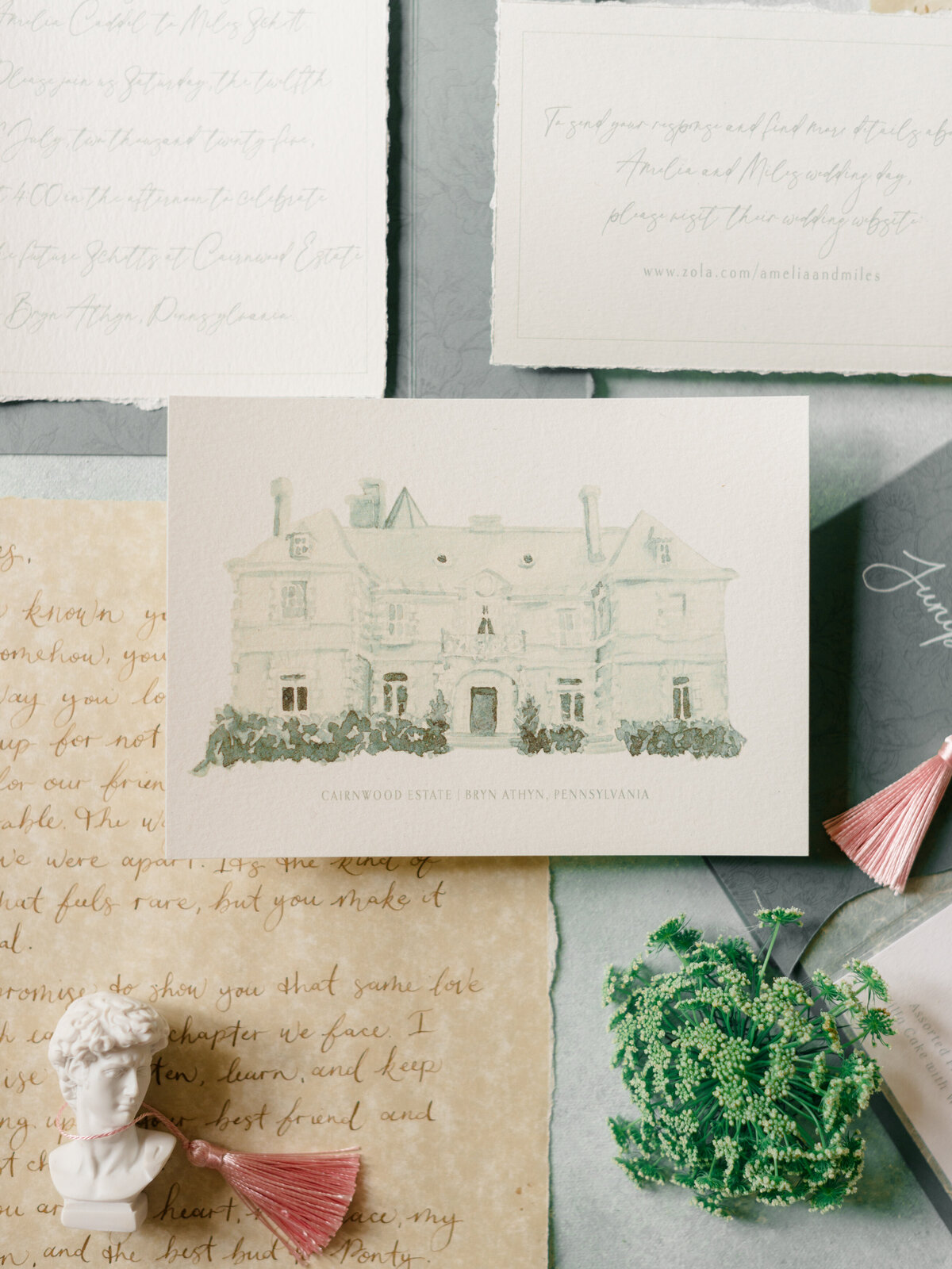 Detail shot of a fine art wedding invitation suite featuring a hand-painted rendering of Cairnwood Estate in Bryn Athyn, Pennsylvania. Styled with vintage accents and soft neutral tones, this image by Elizabeth Kane Photography—Philadelphia Fine Art Wedding Photographer—highlights heirloom wedding paper goods perfect for luxury East Coast celebrations.