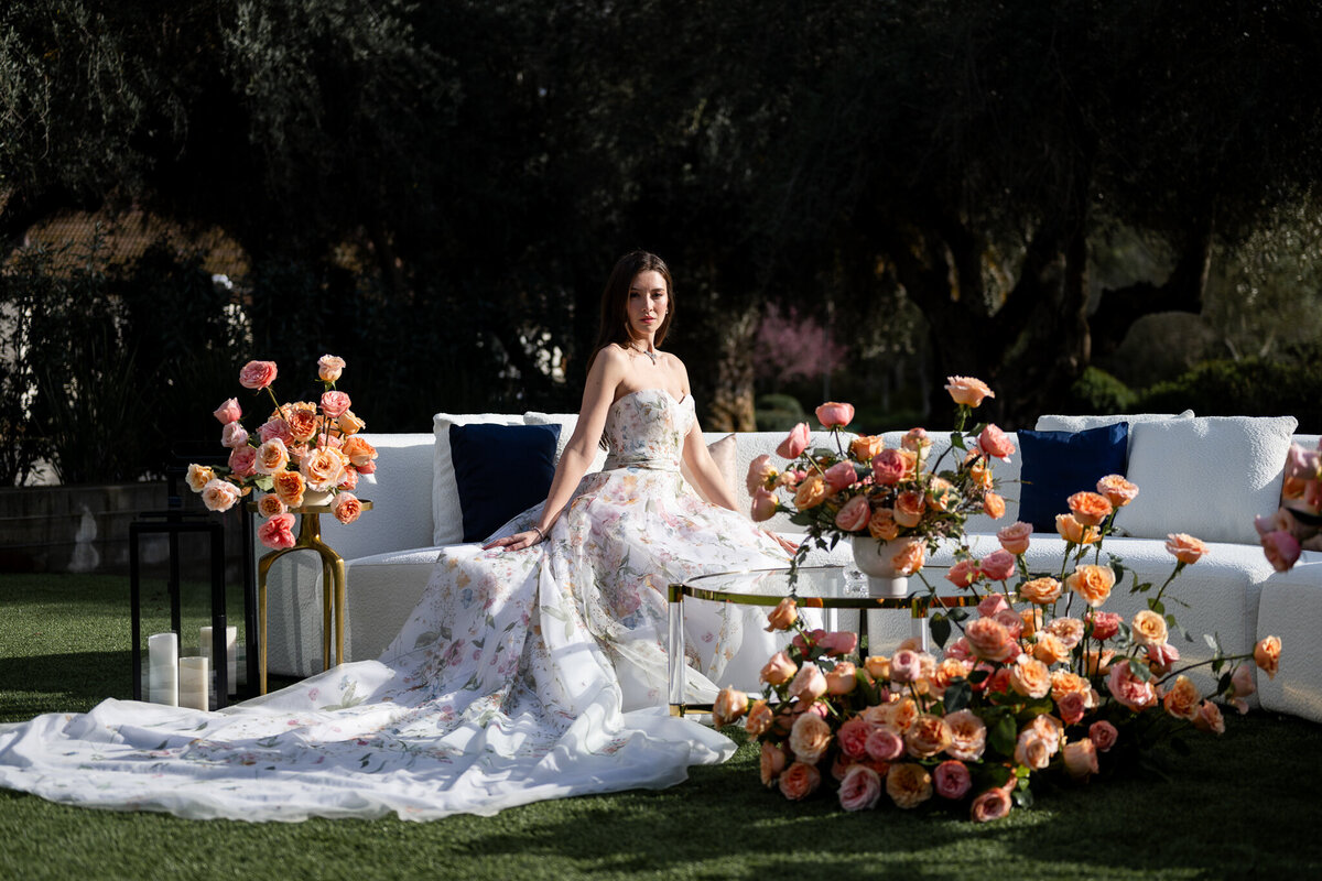 San Francisco Bay Area wedding photographer captures elegant bridal portrait with bride in flowing gown seated among vibrant orange and coral floral arrangements at Estate Yountville in Napa Valley