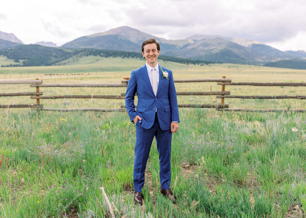 Wearing a vibrant navy suit, the groom smiles at the camera for a groom's portrait