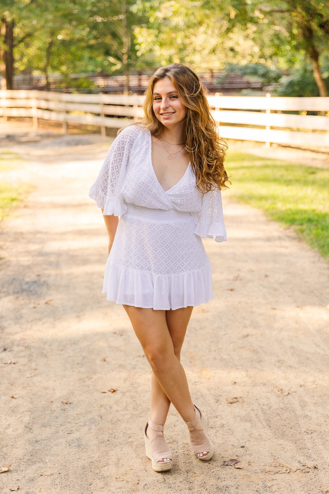 young woman standing in the middle of a park path ankles crossed and hands in the back during senior portraits session
