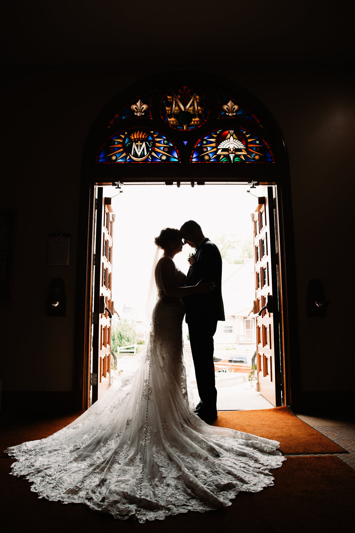 Newlyweds touch foreheads in silhoette in the church entrance doors