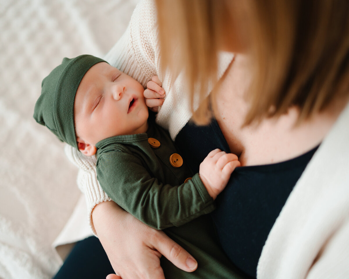 The beauty of natural light maternity photography in Albuquerque with this serene image of a mom gazing lovingly at her sleeping newborn boy. The baby, dressed in a soft green outfit, sleeps peacefully