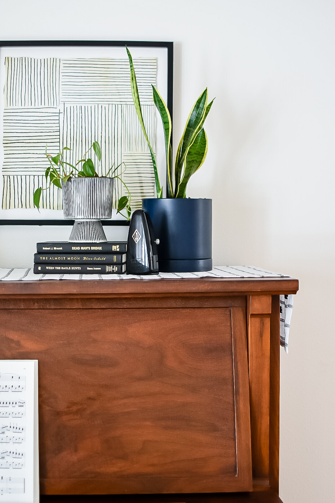 A square abstract art piece hangs on the wall behind a piano