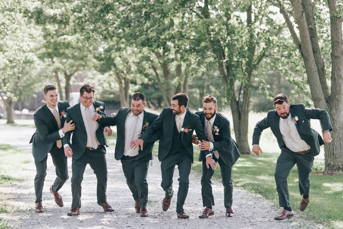 Groom and groomsmen wearing green suits running on a Summer wedding day