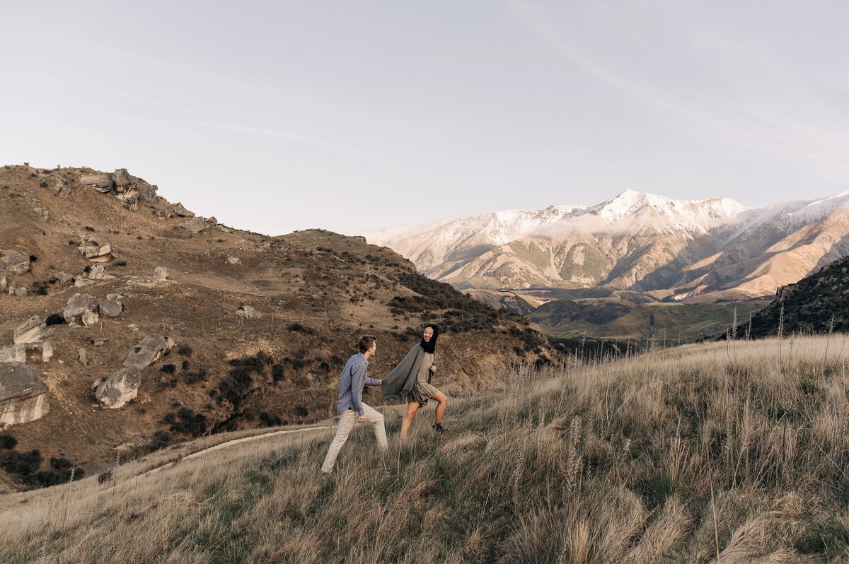 couple hills mountains new zealand christchurch walking engagement wedding romantic hold hands scenic snow long dry grass