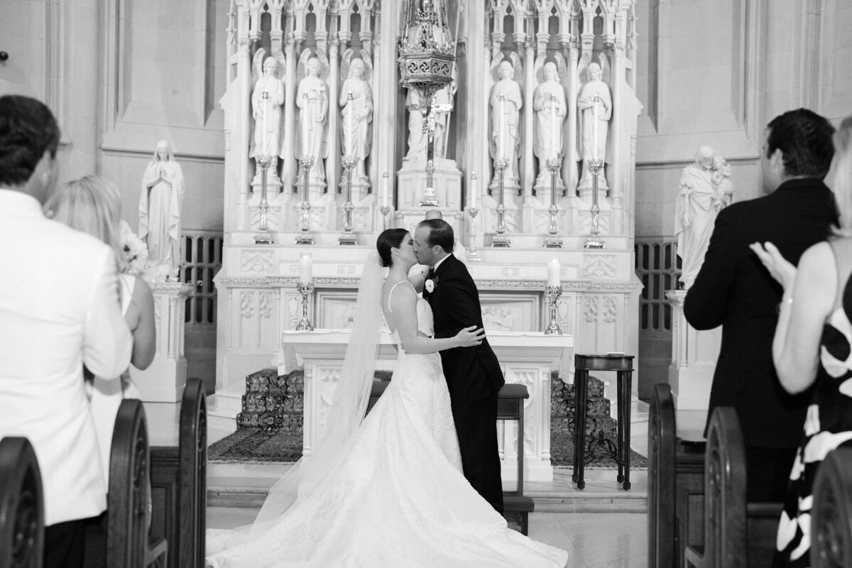 Bride and groom share a kiss at the altar in a beautifully lit church.