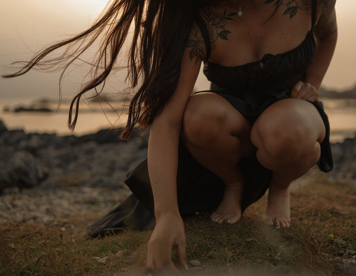 woman in black dress beach combs while the wind gently blows her hair at Oregon Coast