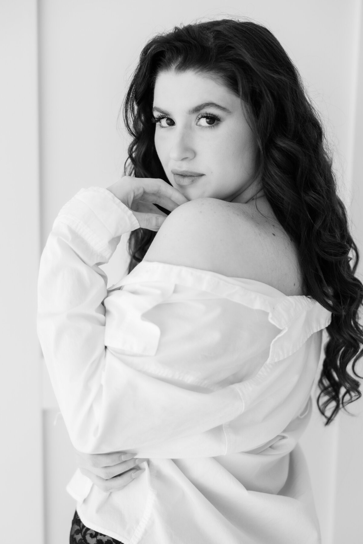 A woman in a white man's shirt in a boudoir photoshoot in black and white.