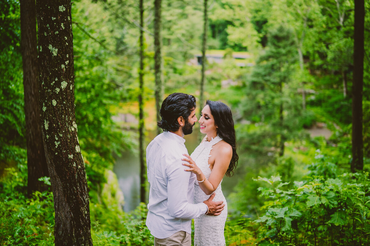 an engaged couple wearing white sharing a moment in a forest of greenery at the property of russel wright called Manitoga
