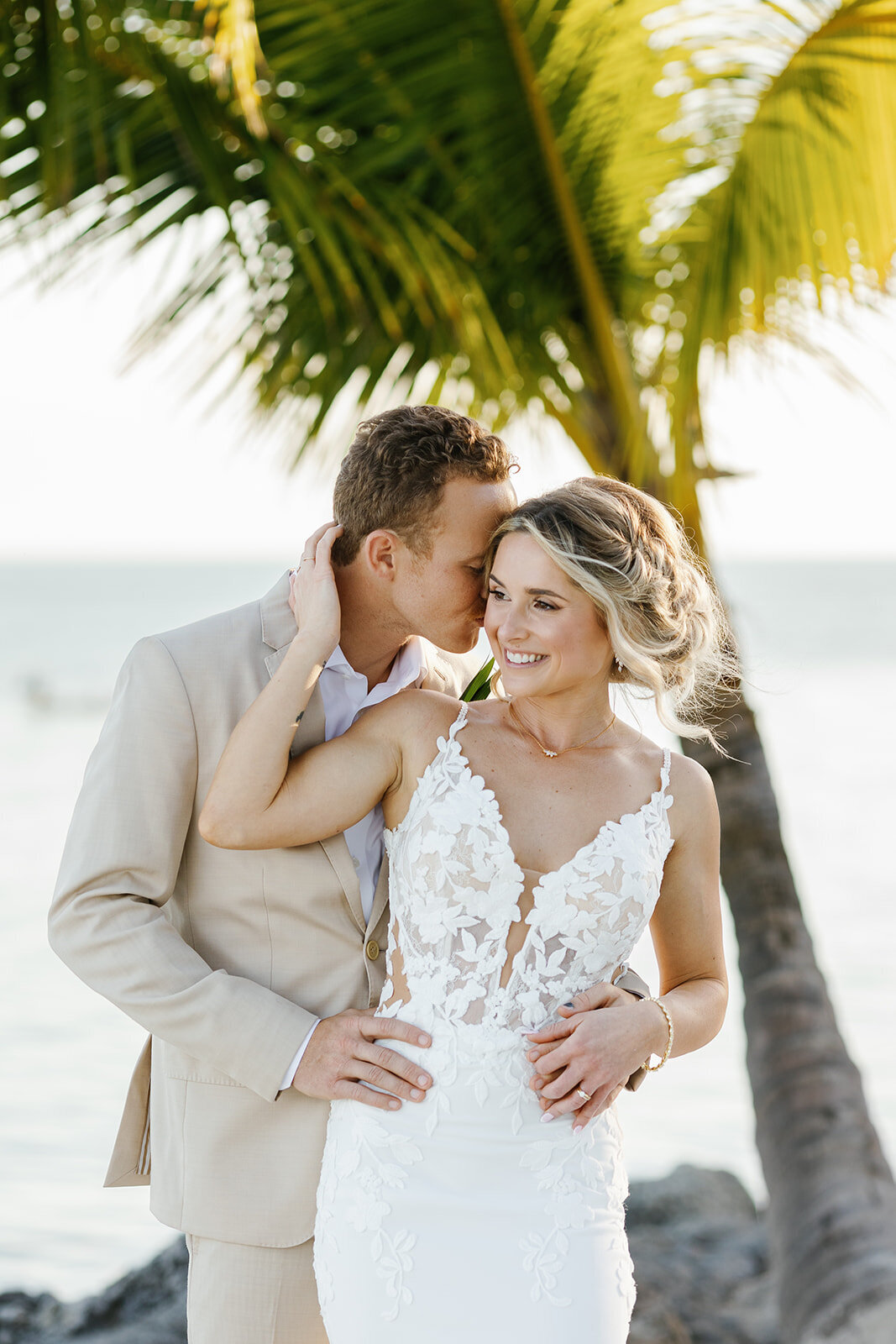 A romantic moment as Hunter kisses Ashley’s shoulder beneath swaying palm leaves.
