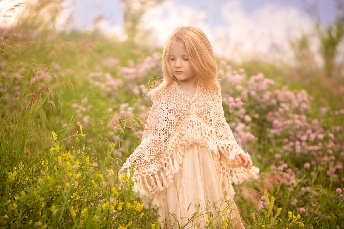 Enchanting portrait of a young girl in a delicate cream gown standing in a sunlit meadow. Captured in Overland Park, Kansas, this scene is perfect for families seeking natural and dreamy child photography.