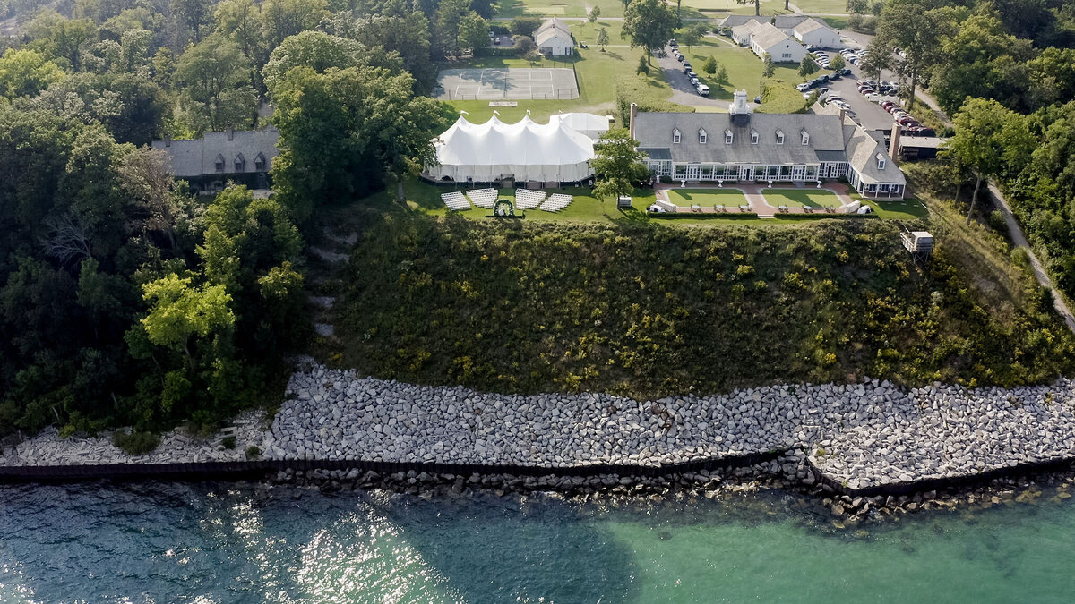 Aerial view of a grand wedding venue by a river, with a large white marquee set up amid green surroundings.