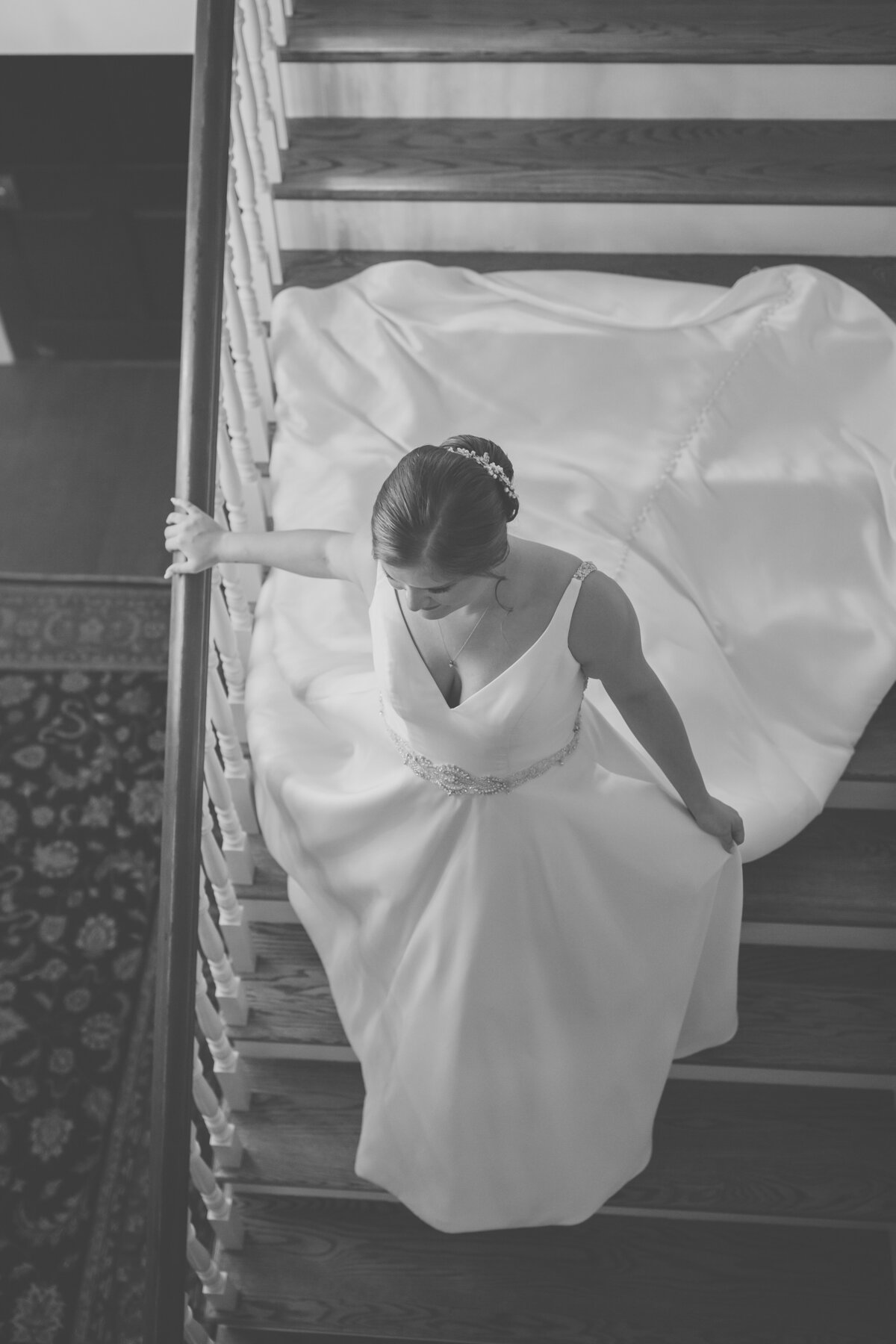 Black and white photo of bride in satin ballgown walking down staircase at historic North Carolina venue.