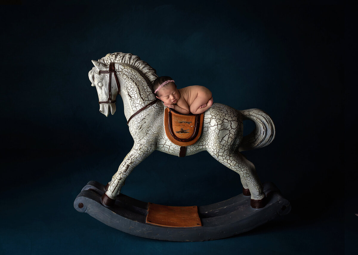 newborn baby laying on rocking horse