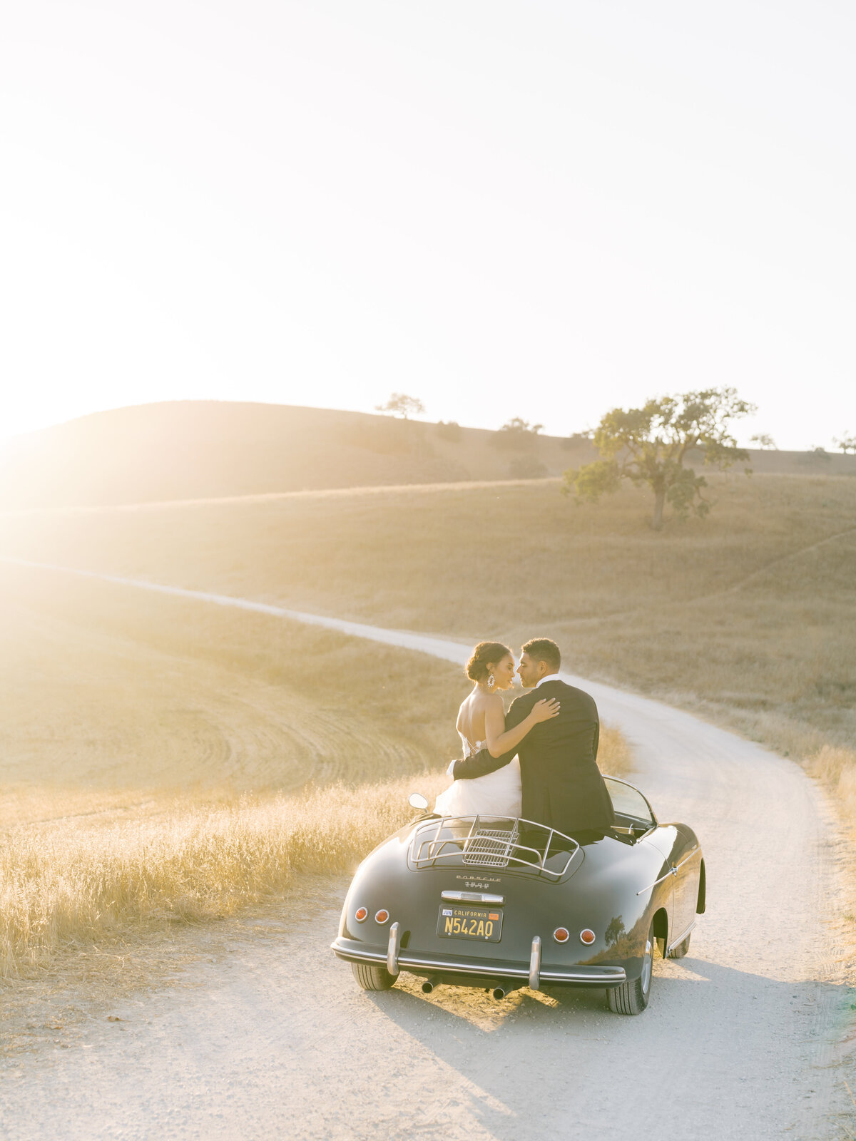 bride and groom sitting on vintage car at sunset