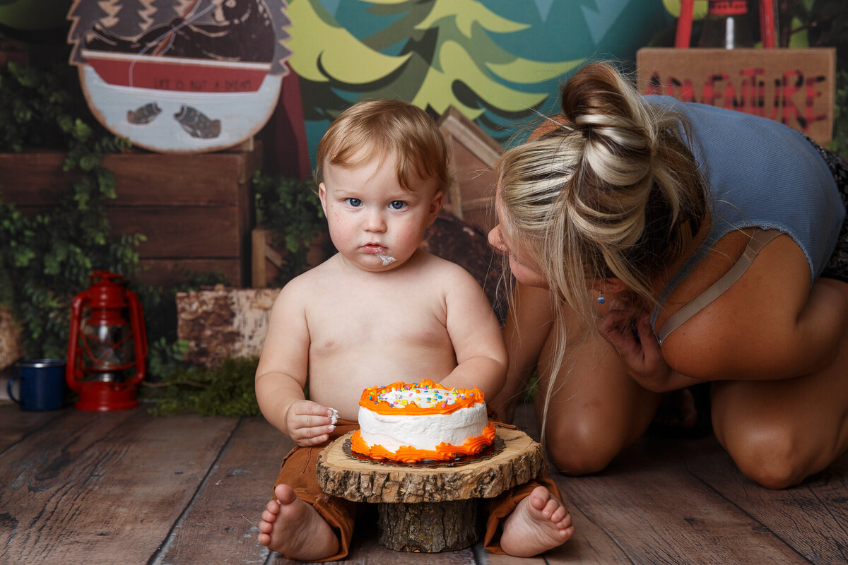 Mom leaning over her one year old baby during a  first birthday cake smash