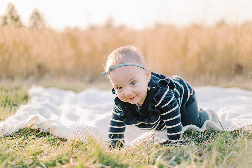 Baby crawling on a white blanket in a field of yellow grass
