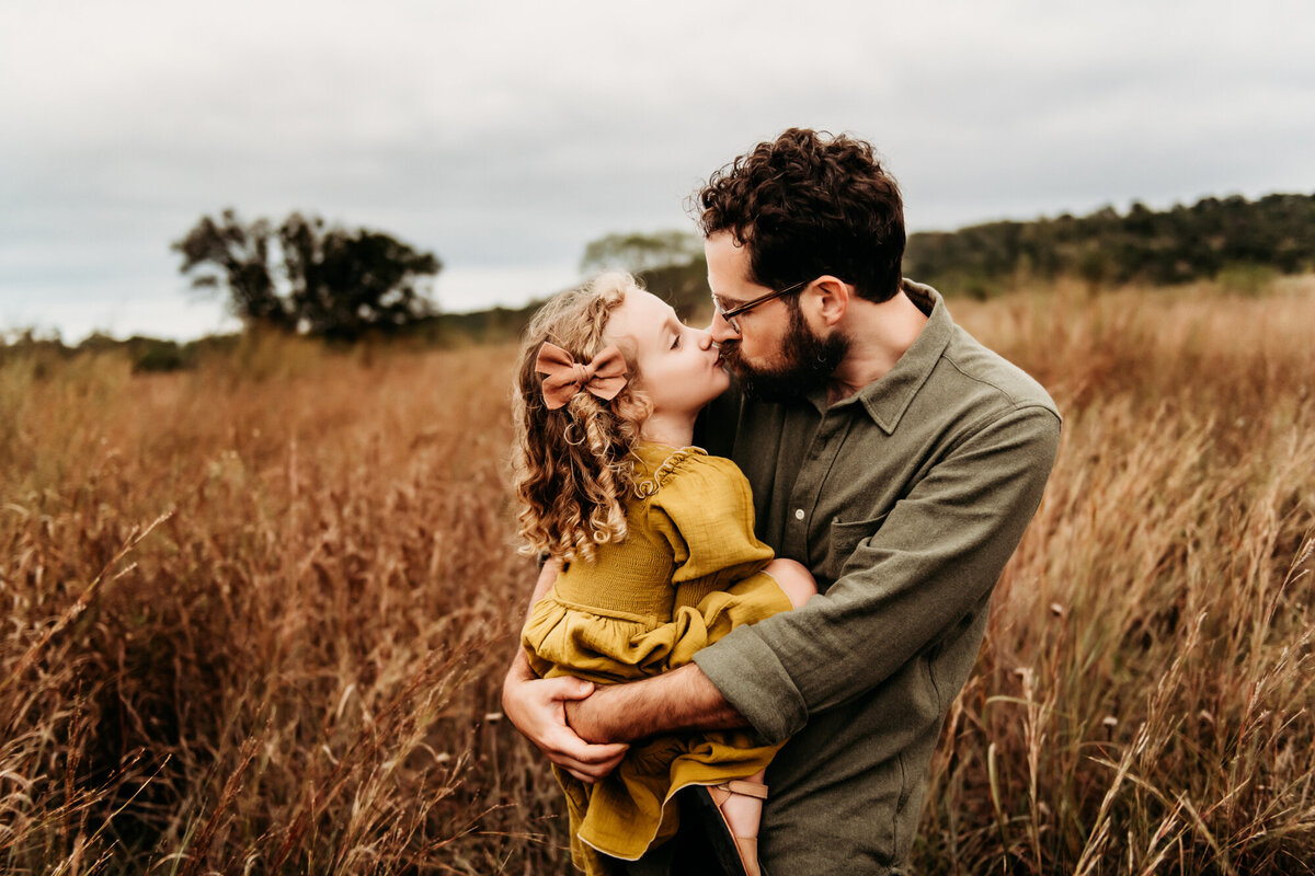 Family Photographer, Dad snuggling little girl in a yellow dress in the field.