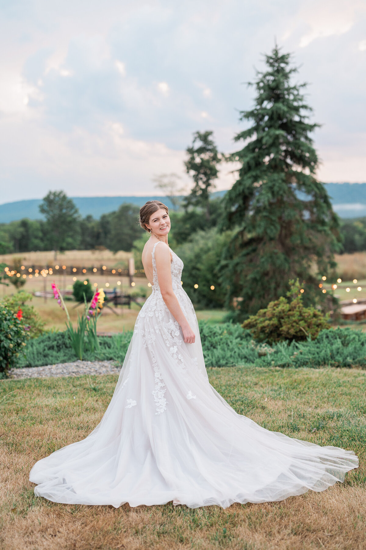 A bride standing in a grassy field looking over her shoulder