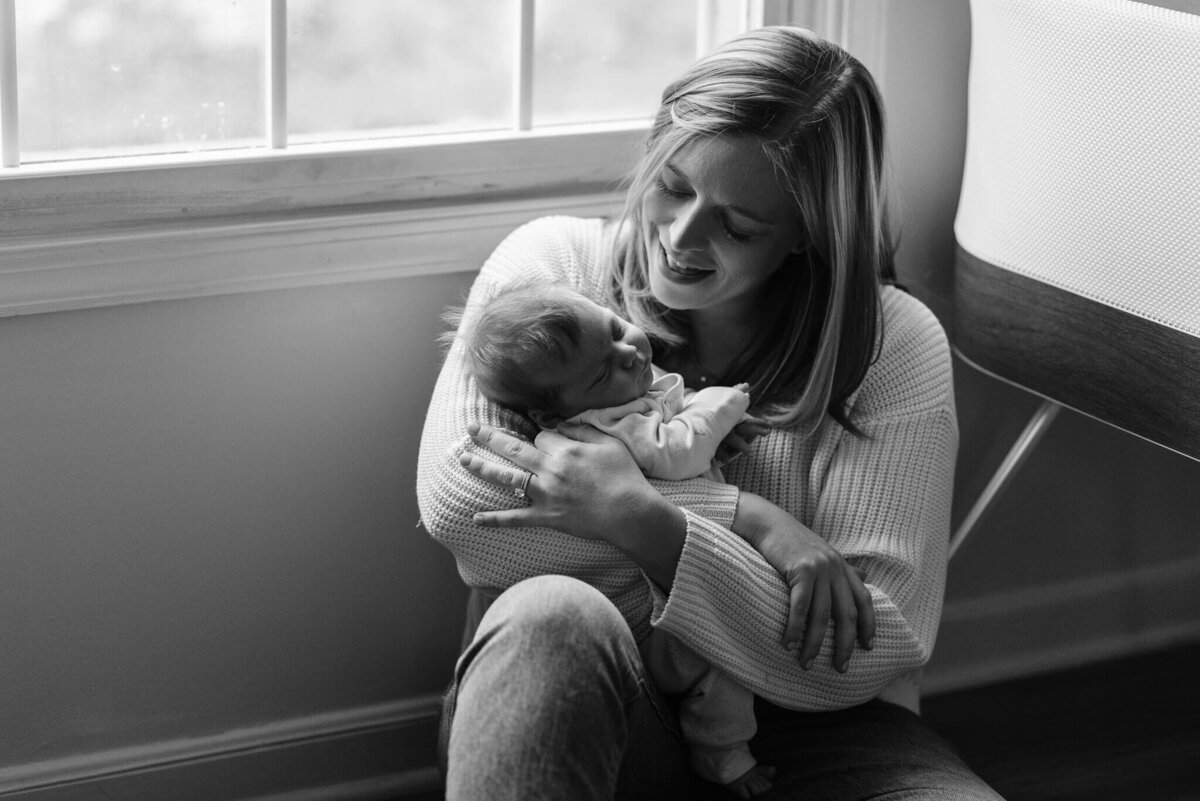 B&W newborn photography of a mom and her twin boy under a window