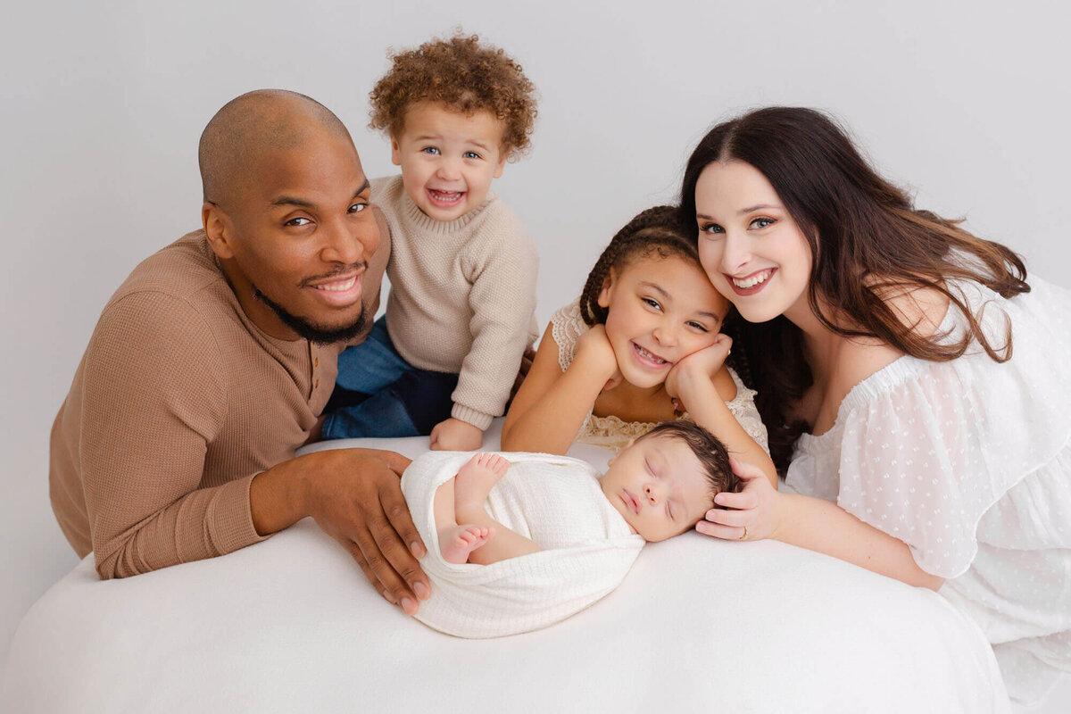Family of 5 with newborn baby, everyone is smiling and looking at the camera. Everyone is wearing light, neutral tones and colors.