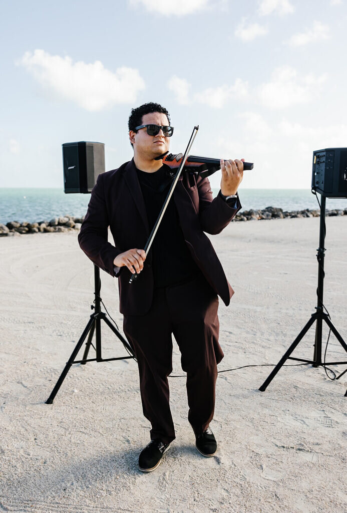 A professional violinist plays live music against the stunning ocean backdrop of a Florida Keys destination wedding. Captured by Claudia Amalia Photography.