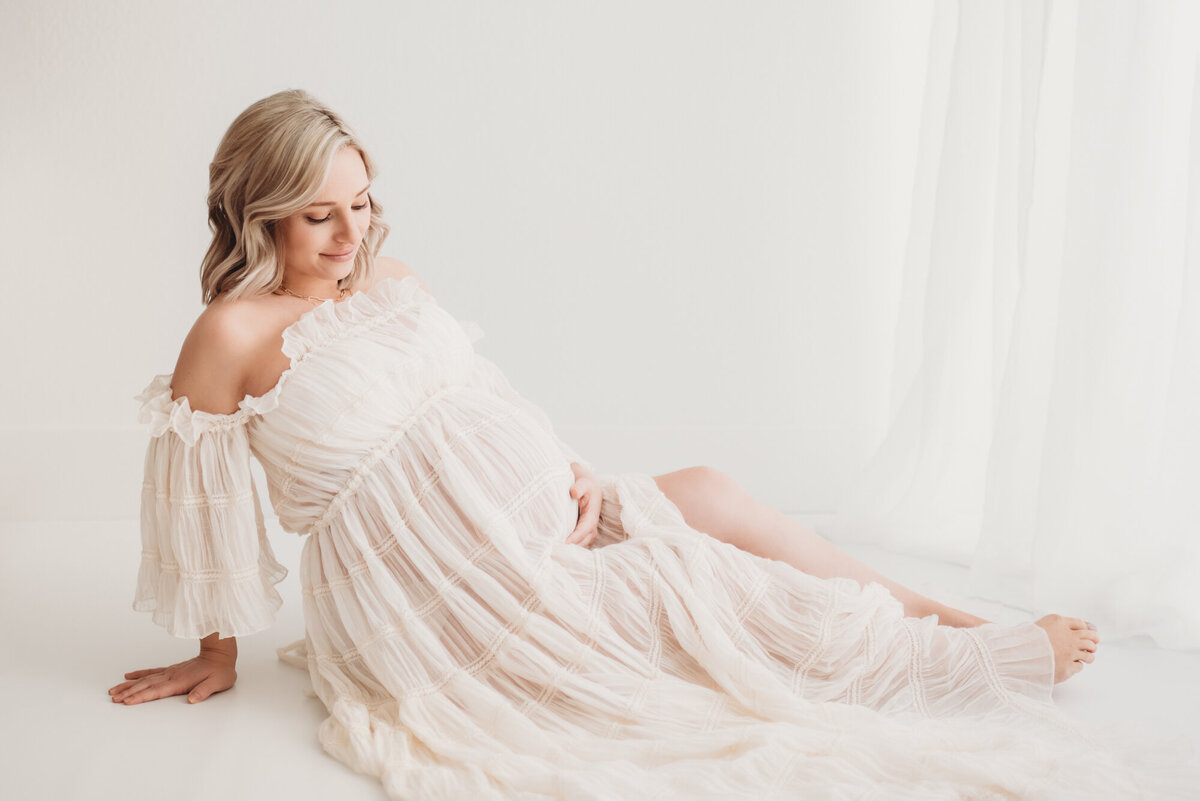 pregnant woman sitting on floor of white studio with legs outstretched