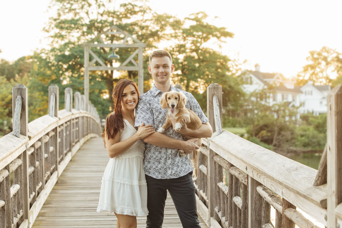 Couple holding their dog on a bridge during sunset engagement photo in Spring Lake New Jersey