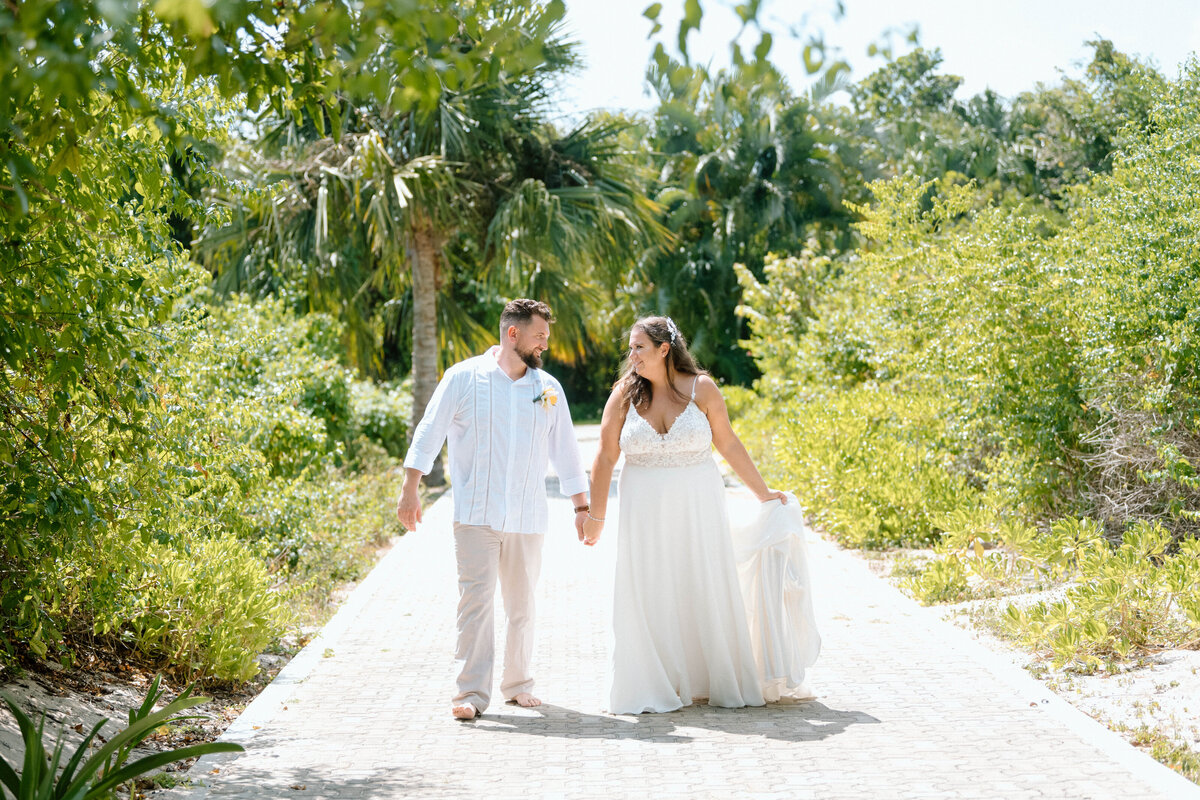 a bride and groom walk a palm tree lined path