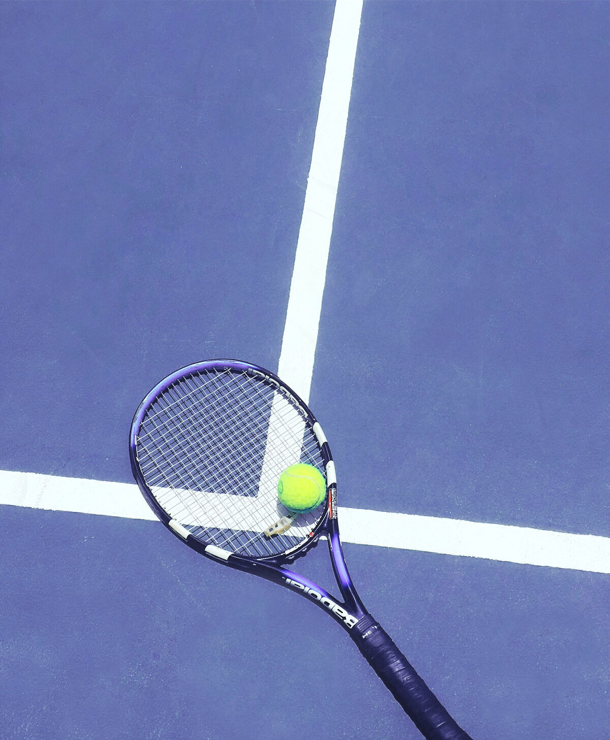 Raquette de tennis avec une balle posée dessus reposant sur un terrain en dur bleu et blanc.