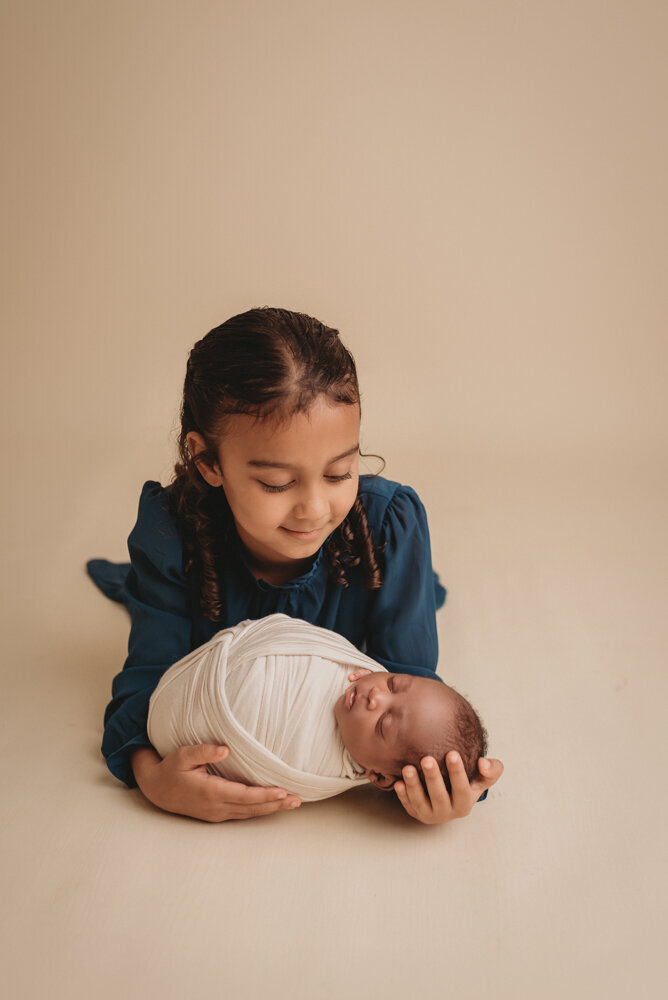 Newborn photos with Atlanta, Georgia newborn photographer of sleeping baby boy with hands under chin wrapped in cream swaddle being held by his mom, dad and big sister.