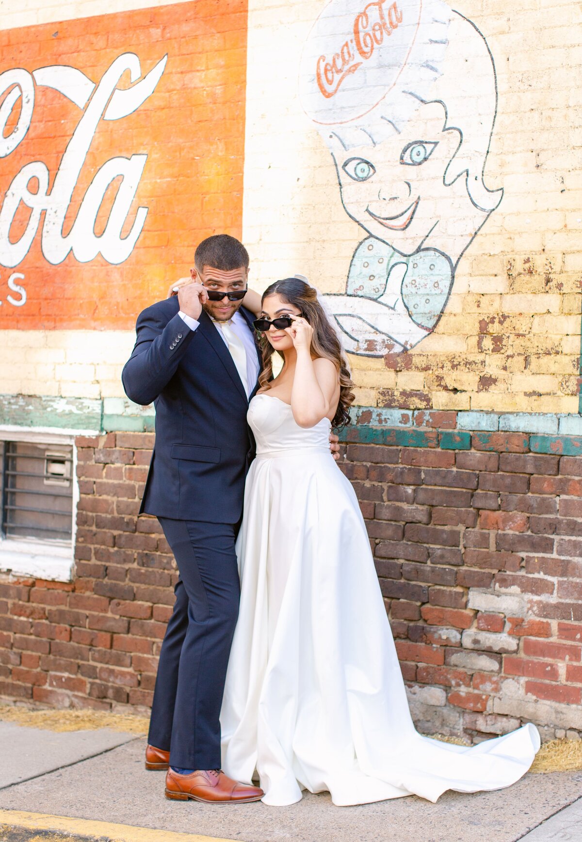 Bride and groom peeking through sunglasses in front of a brick wall in Culpeper, Virginia.