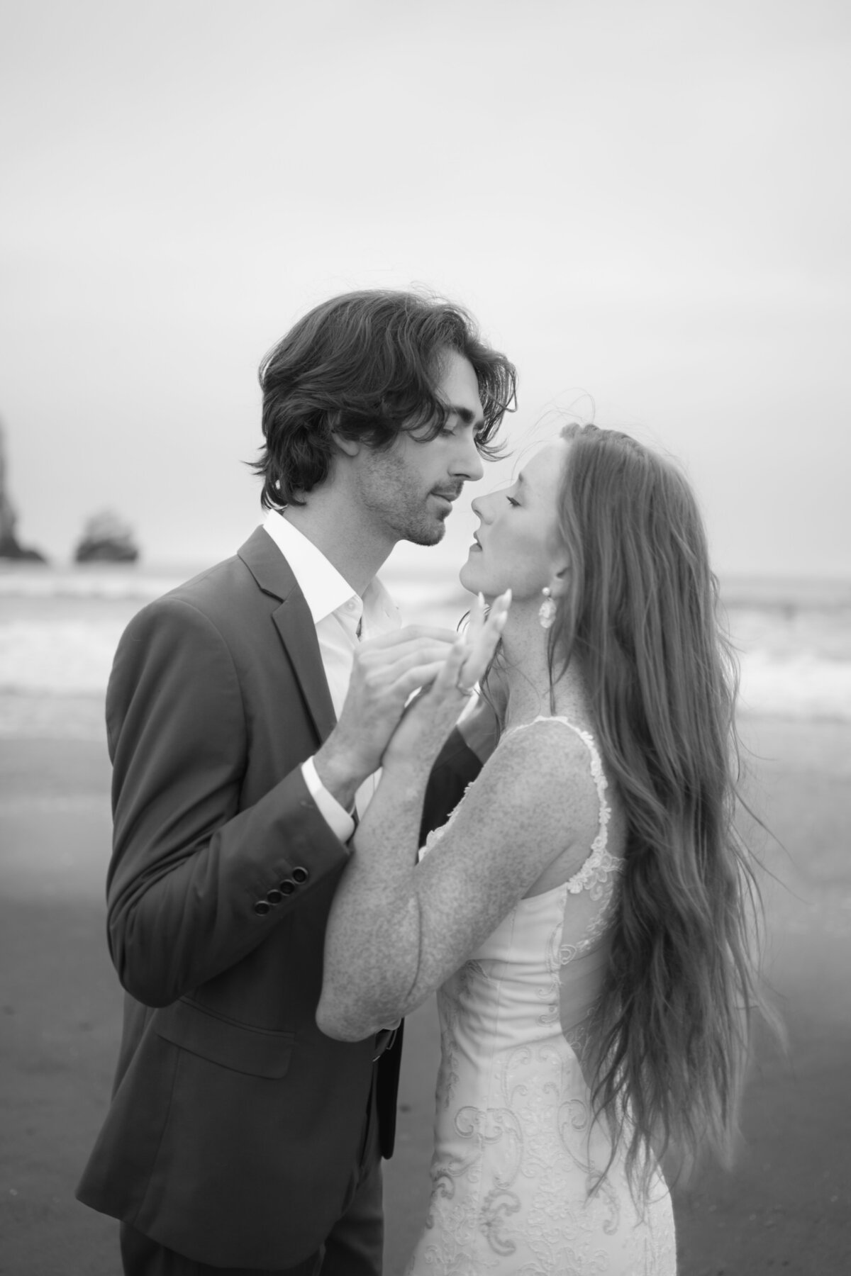 Closeup black and white portrait of the bride and groom on the beach in Morro Bay, California caressing each other's hands