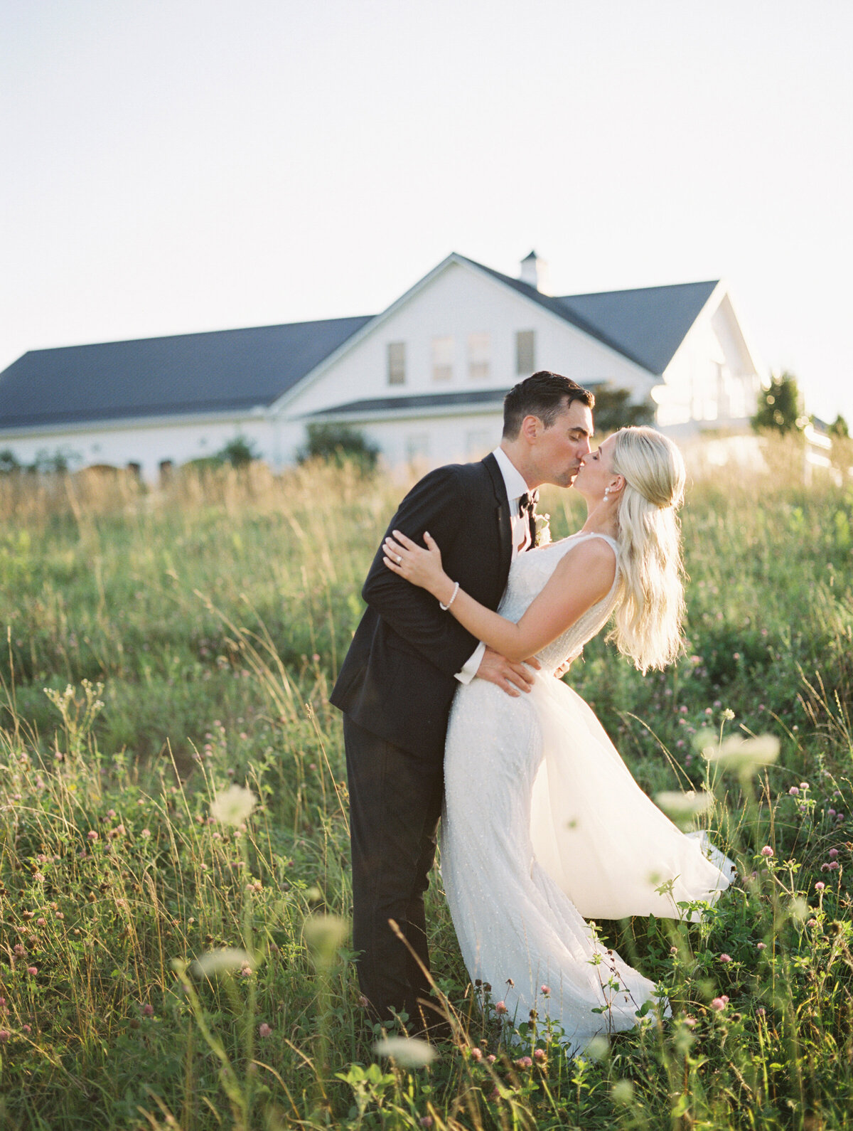 photo of bride and groom kissing in a field in front of their venue taken by Mansfield Wedding Photographer, Annie Trammel