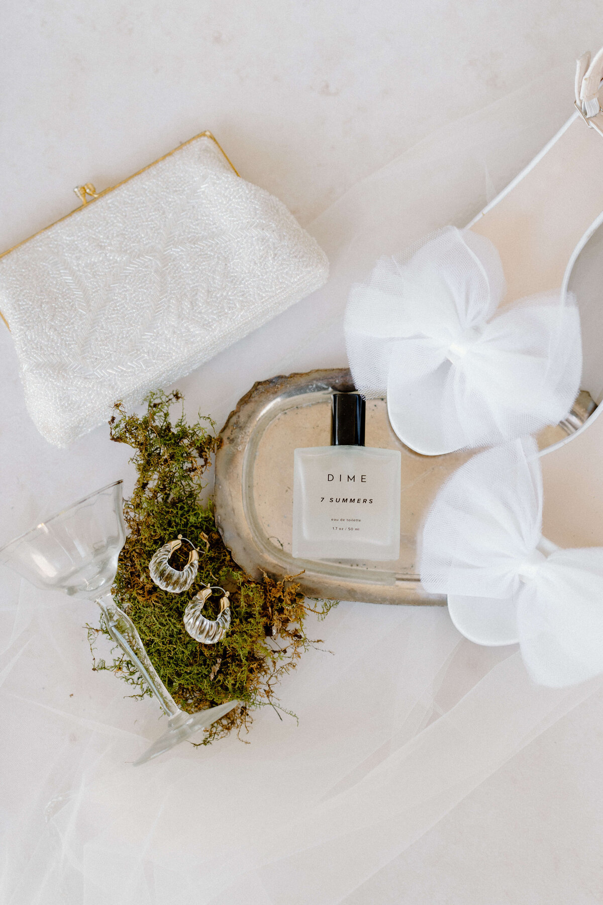 wedding details including white shoes, perfume, earrings and clutch