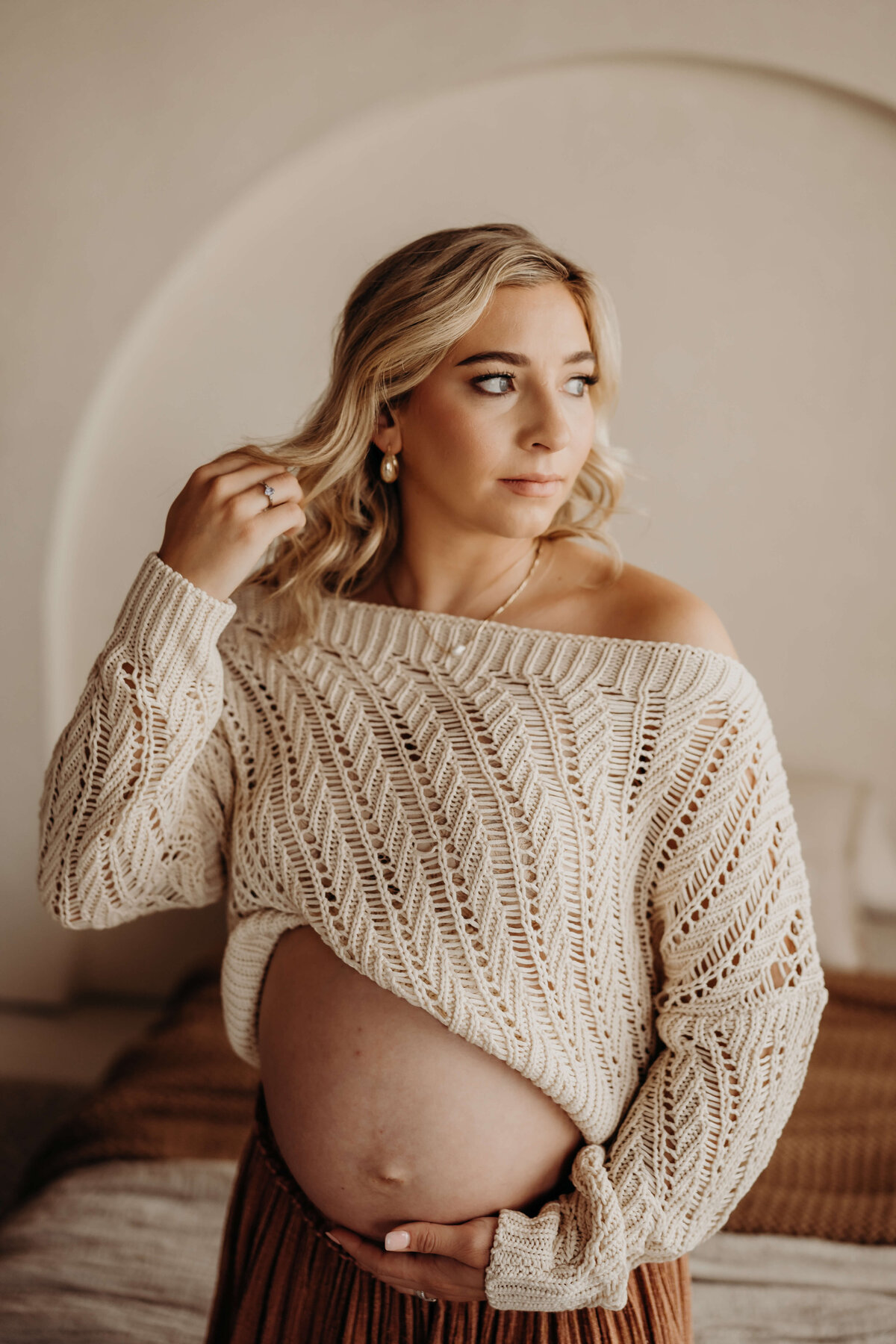 pregnant woman plays with hair wearing crochet cream sweater
