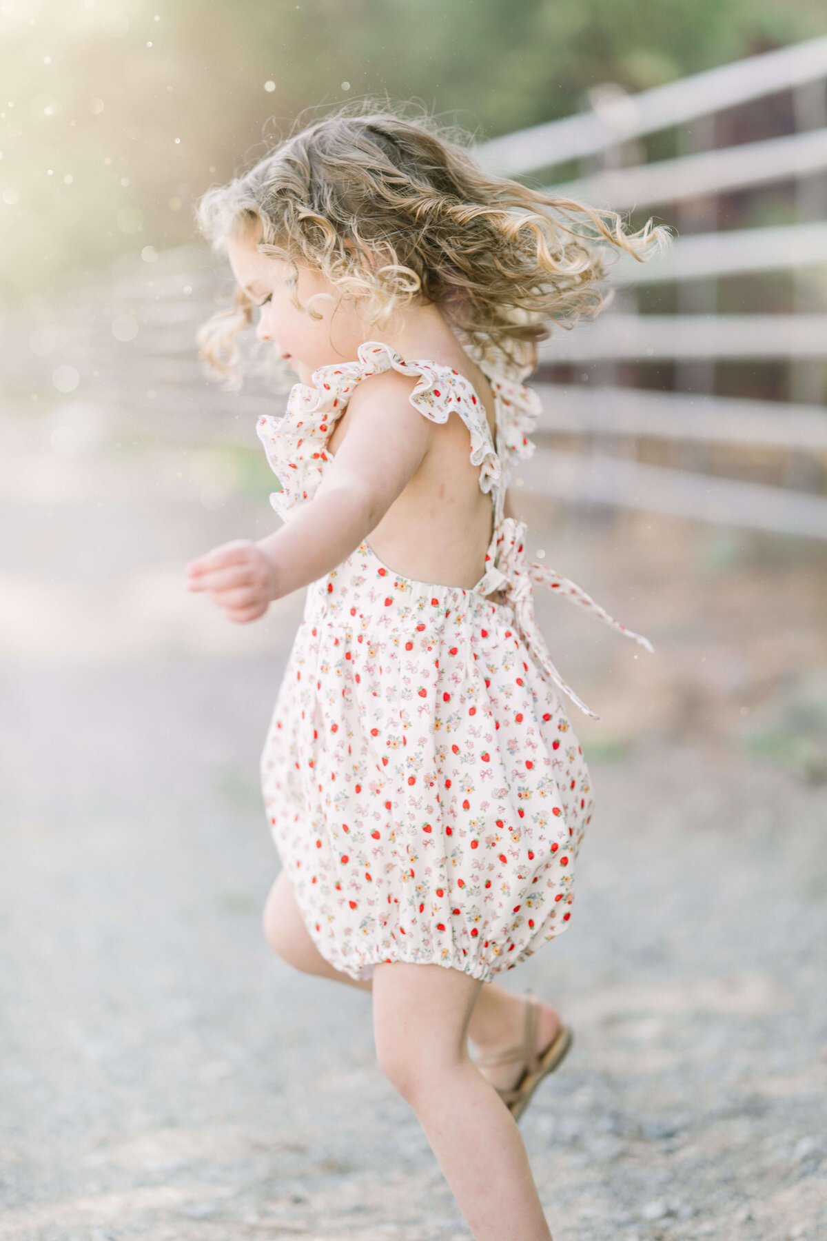 Young toddler with curly hair twirls in  strawberry bubble.