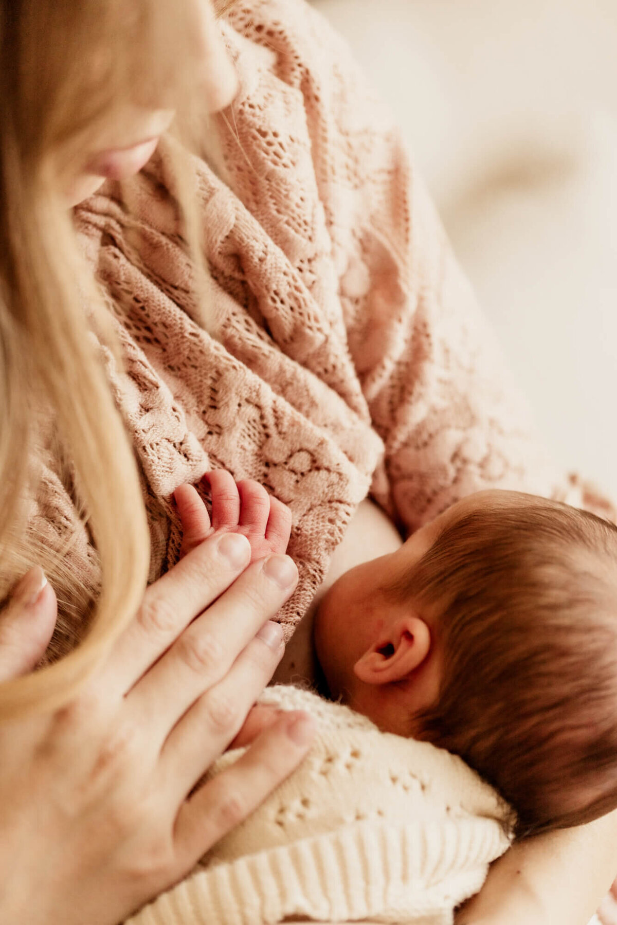Close up photo of a mother breastfeeding her baby girl with her hand placed on her baby's hand.