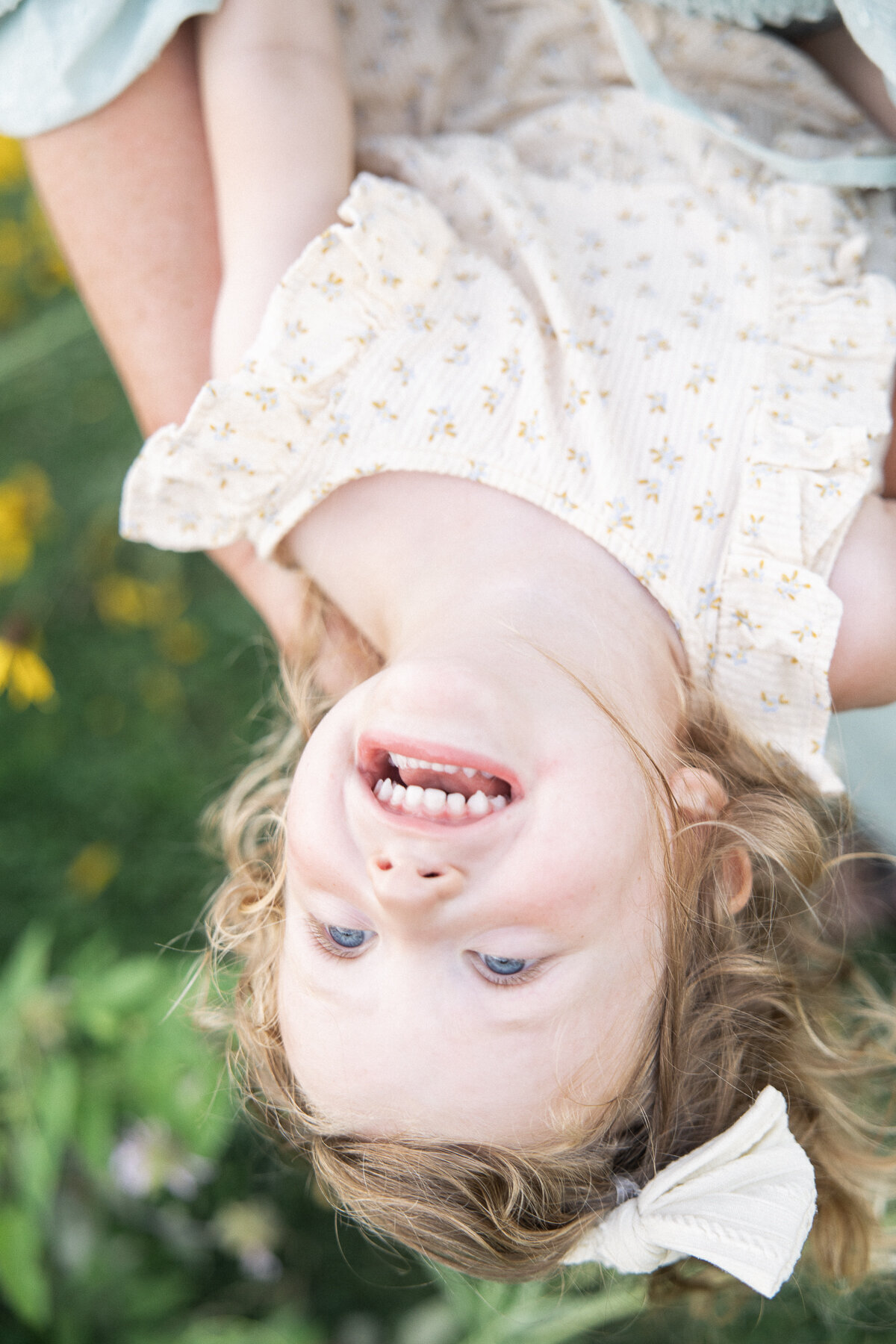 Young girl in cream yellow floral dress giggles while upside down during Indianapolis family pictures
