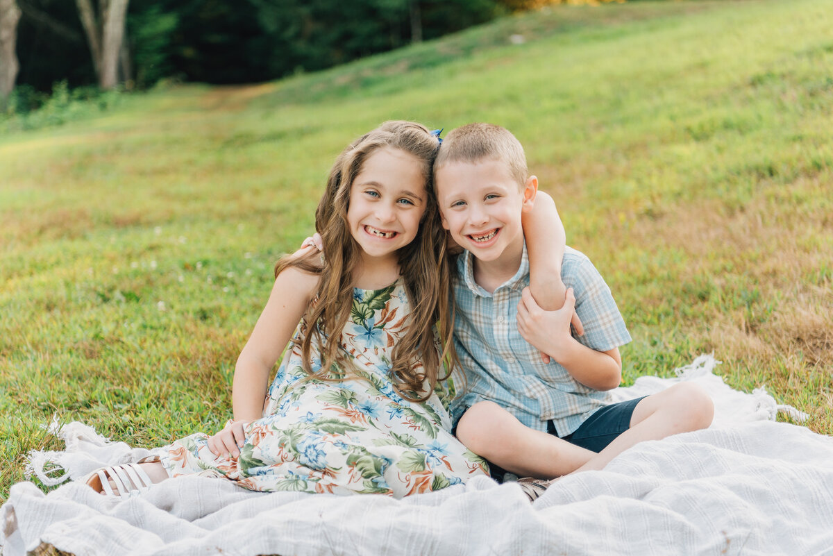 Brother and sister smiling at camera, sitting on a blanket