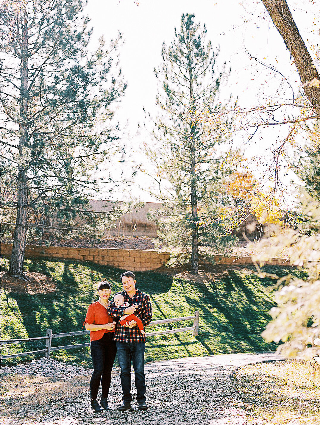mom and dad hold baby son at park in fall