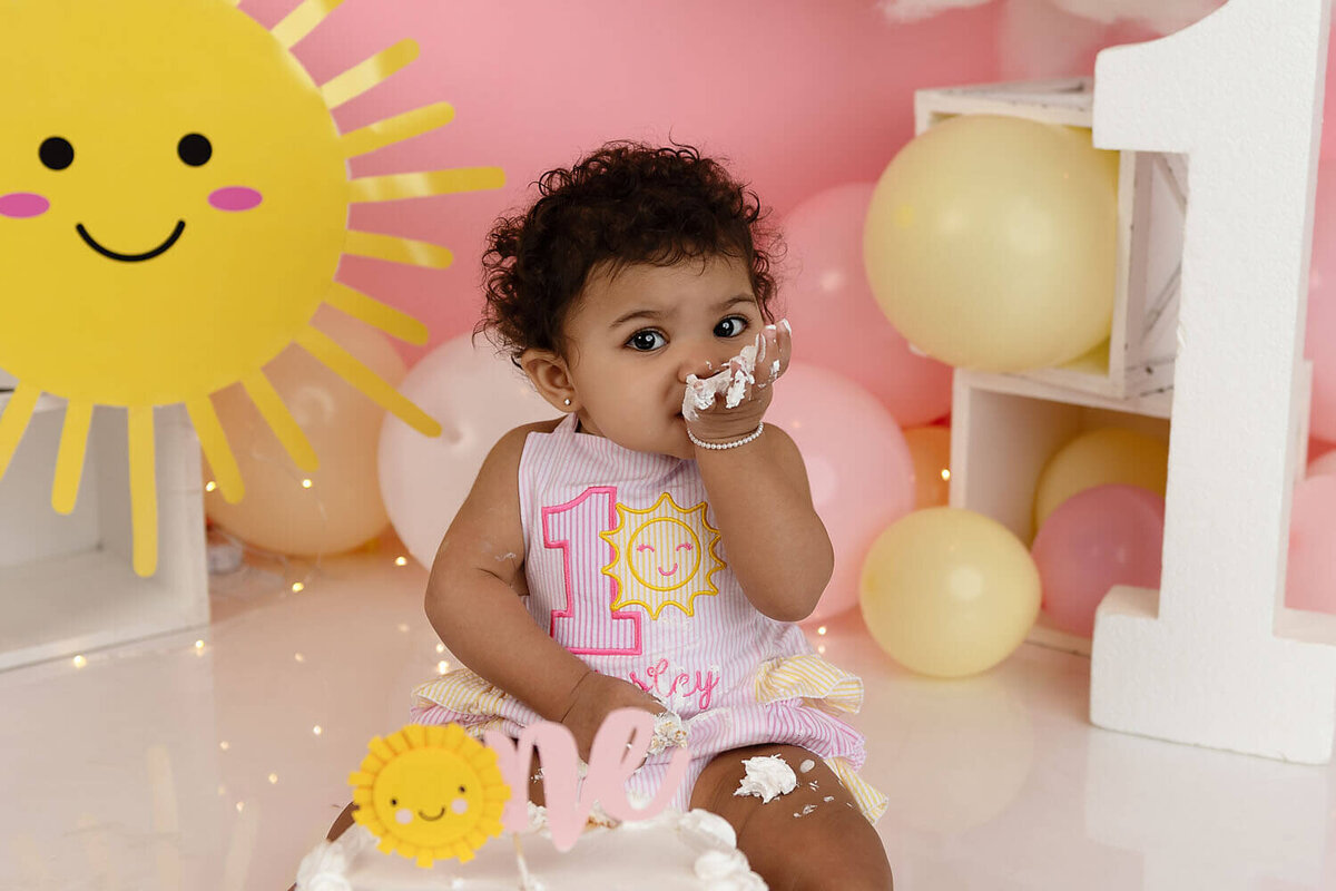 A happy toddler eats cake during her first birthday cake smash photo session