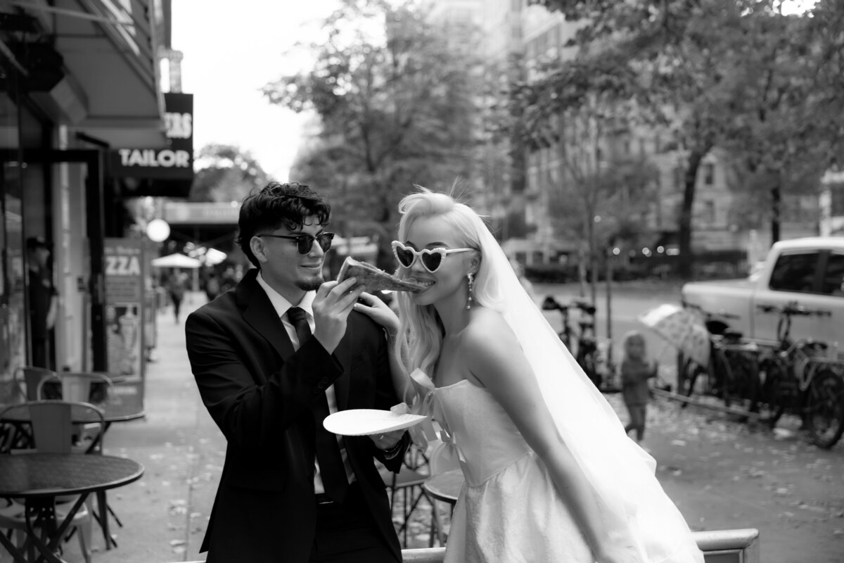 Bride and groom toasting their pizza slices together in celebration of their NYC elopement.