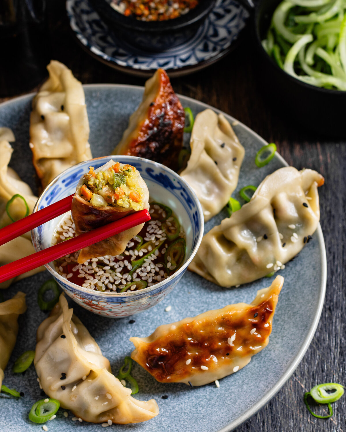 Vegetable gyoza held over a dip bowl with chopsticks surrounded by other pan fried gyoza